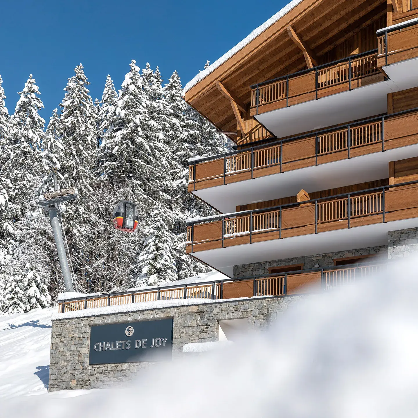 Vue extérieure des Chalets de Joy au Grand-Bornand en hiver, avec le télécabine de la Joyère