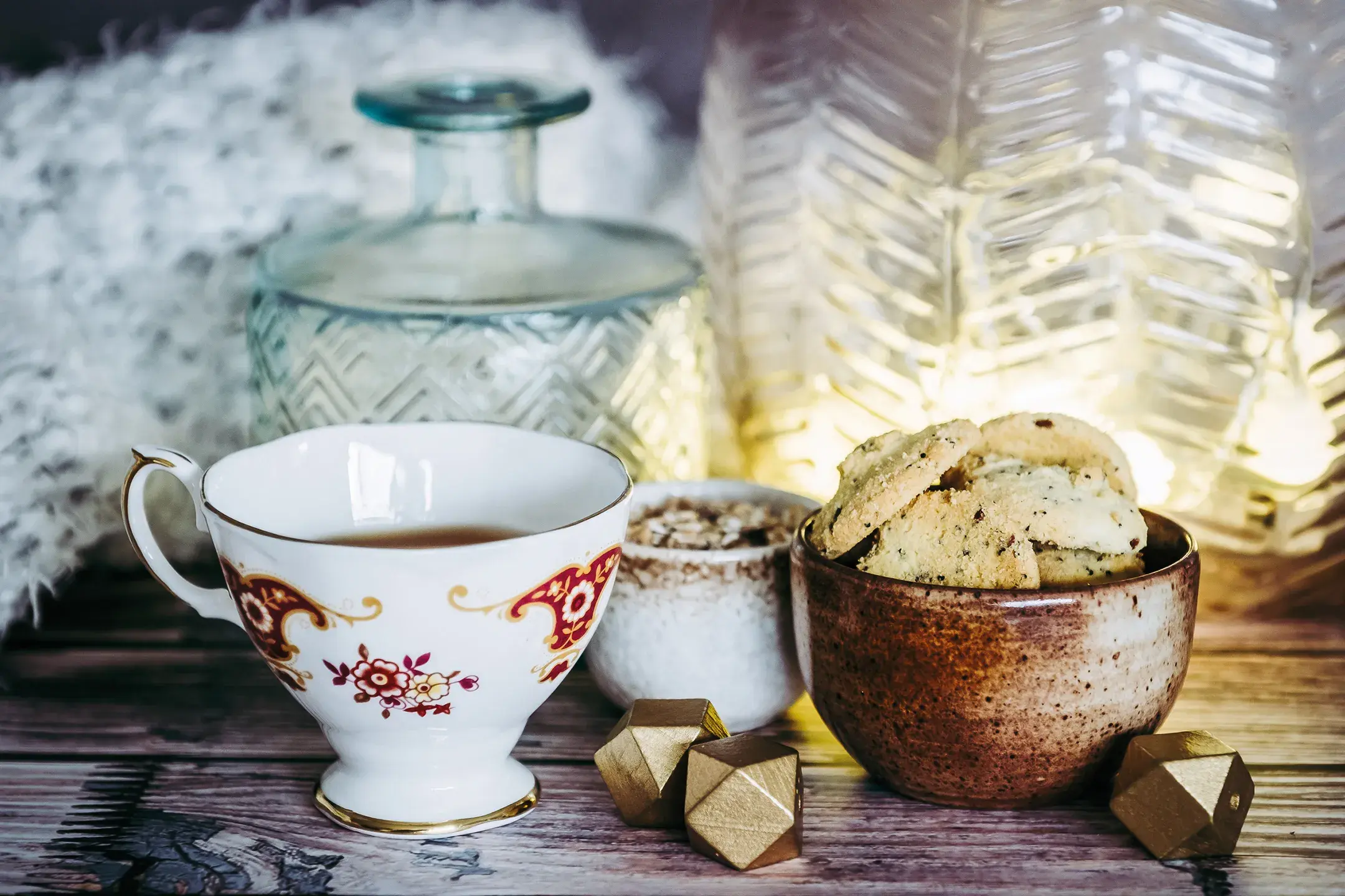 Une tasse de thé et des cookies sont déposées sur une table, à côté de vases et d'un plaid en laine