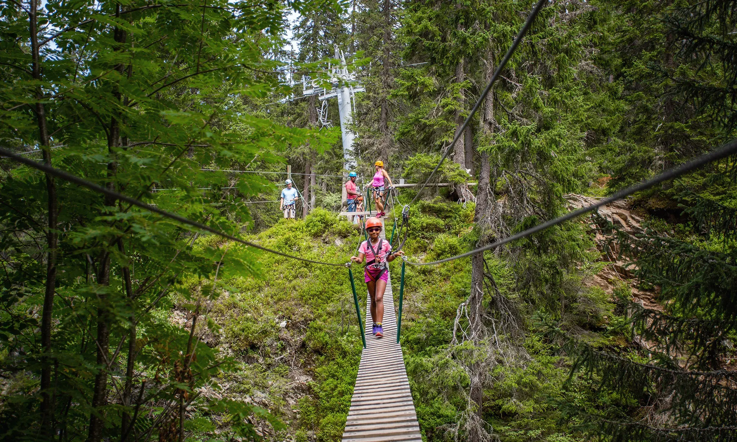 Une petite fille est en train de traverser un pont suspendu en accrobranche aux Saisies