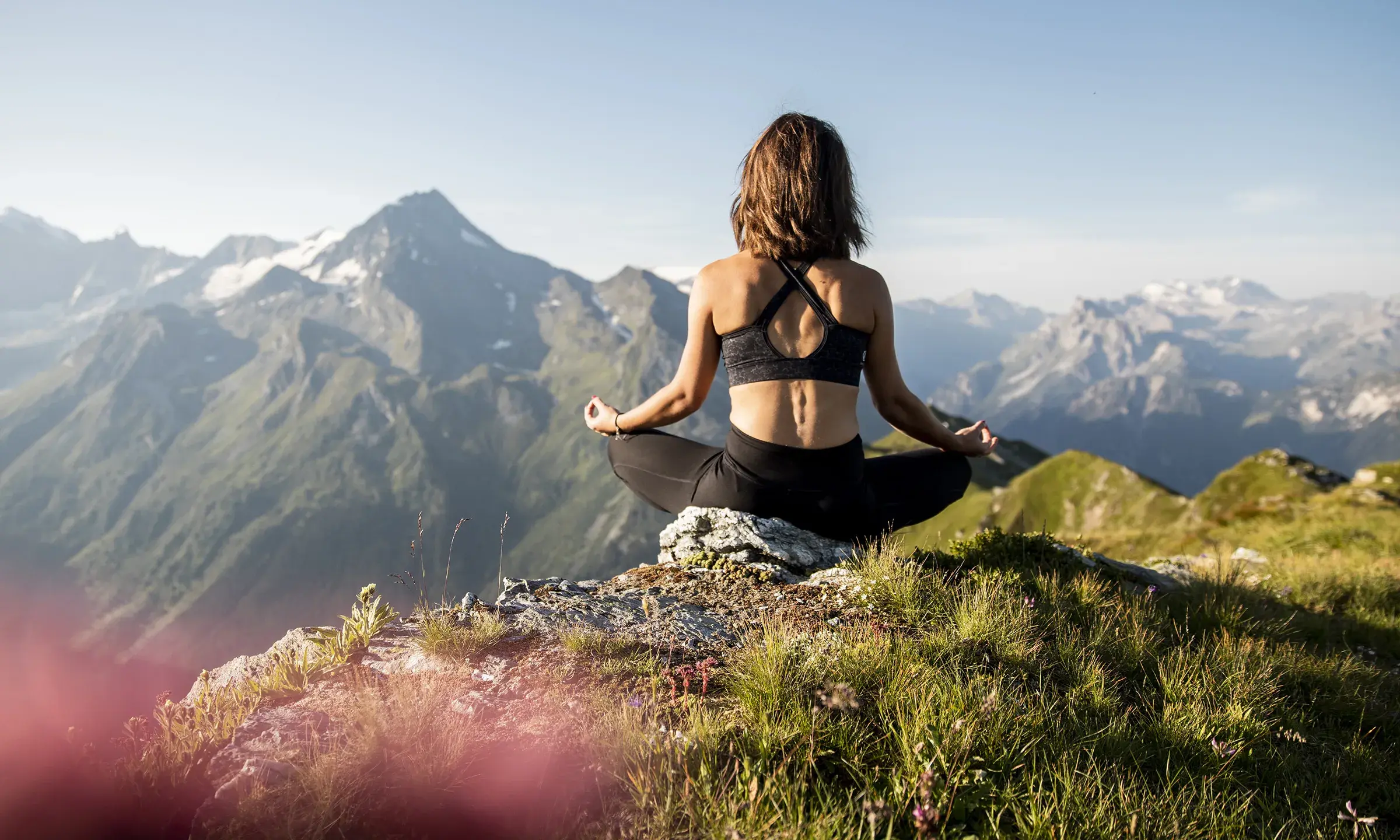 Une femme est en train de faire du yoga au sommet d'une montagne avec  une magnifique vue sur les massifs environnants