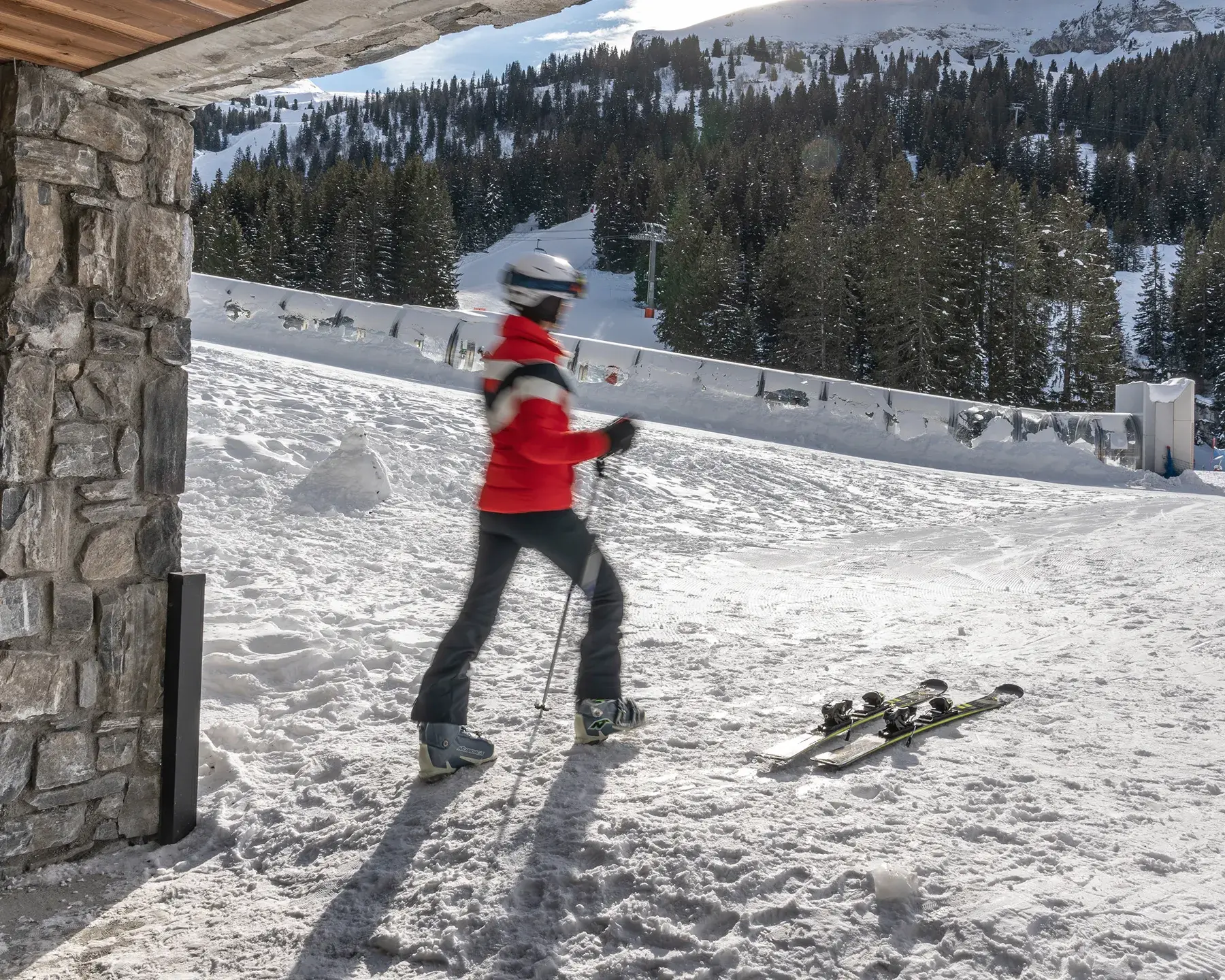 Femme qui chausse ses skis sur le front de neige de Flaine à la sortie du skiroom de la résidence Alhéna